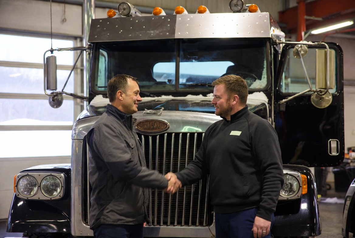 A proud American truck owner shaking hands with a mechanic beside a gleaming, winter-ready diesel truck. Warm shop lighting contrasting with snowy windows in the background, 8K realism, themes of trust and reliability.